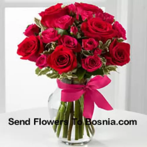 18 Roses Rouges avec des Remplissages de Saison dans un Vase en Verre Décoré d'un Nœud Rose